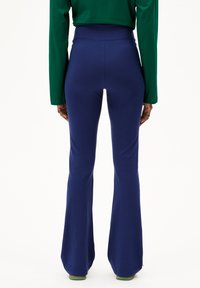 Hoge taille, flared broek in marineblauw, met een gladde textuur en rekbare stof, van achteren getoond met een groene top met lange mouwen.