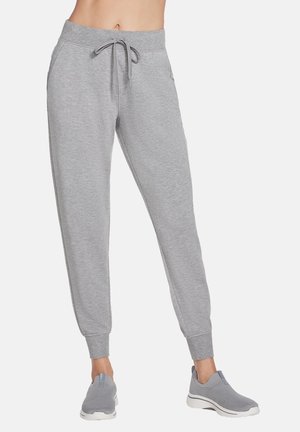 Graue Sweatpants mit einem Kordelzugbund, seitlichen Taschen und Rippbündchen, kombiniert mit grauen Schlupfschuhen.