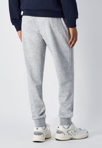 Lichtgrijze sweatpants met elastische boorden, gemaakt van zachte stof, gecombineerd met witte sneakers met zwarte accenten.