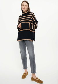 Zwart en beige gestreepte coltrui met oversized mouwen, gecombineerd met lichtgrijze jeans en bruine loafers. Soepele stof en losse pasvorm.