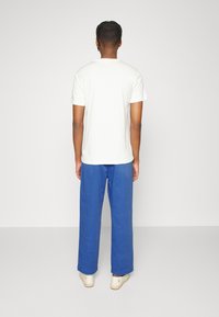 Vit kortärmad t-shirt i kombination med löst sittande, blå linnebyxor. Outfiten har en avslappnad passform och kompletteras av ljusa skor.