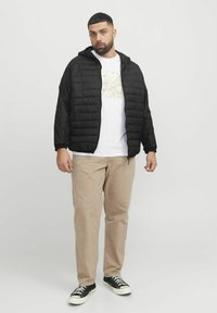 Black puffer jacket with a hood, featuring a quilted design. Paired with a white graphic t-shirt, beige pants, and black sneakers.