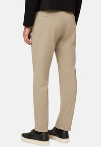 Pantalones beige de tela suave con corte ajustado, que cuentan con bolsillos traseros y un diseño clásico, combinados con zapatillas negras de lona bajas.