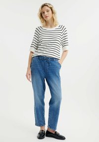 Gestreepte, witte en zwarte top met korte mouwen en ronde hals, gecombineerd met losse, lichtblauwe denim broek met elastische tailleband en zakken.