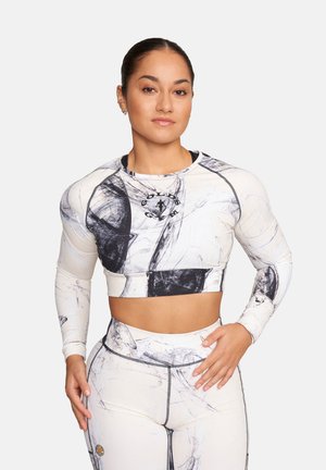 Kobieta ubrana w biało-czarny, marmurkowy, długi rękaw krótki top i legginsy z wysokim stanem, stojąca z rękami na biodrze i udzie.