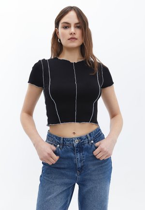 T-shirt nero corto con maniche corte, caratterizzato da linee di cucitura bianche in contrasto, un collo rotondo e bordi grezzi. Indossato con jeans blu a vita alta.