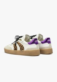 Sneaker bianchi con strisce a stampa leopardata, lacci neri trasparenti, punte metalliche viola e suole beige su uno sfondo bianco.