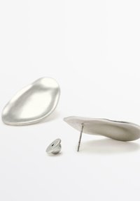 Accessori in metallo argentato includono due pezzi lisci e ovali, uno con un perno e l'altro con un elemento di chiusura distintivo.