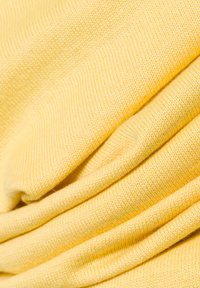 Gelbes Strickgewebe mit einer weichen Textur, das gleichmäßige Falten und ein einheitliches Webmuster aufweist und somit ein gemütliches Erscheinungsbild schafft.
