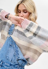 Sweter dziergany w poziome paski w beżu, szarości i różu; zestawiony z dżinsowymi ogrodniczkami z regulowanymi szelkami i przednią kieszenią.