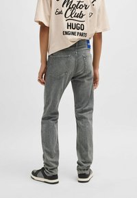 Grå denim jeans med rak passform, bakfickor och sömdetaljer; kombinerat med svarta sneakers. Bakifrån av klädseln.