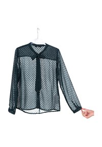 Blouse transparente verte foncée avec un col et un détail de nœud, ornée d'un motif à pois et à manches longues, présentée sur un cintre.