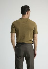Polo de manga corta verde oliva con cuello clásico, combinado con pantalones oscuros a rayas con bolsillos traseros y cierres.