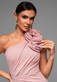 Abito rosa a spalla unica con applicazione floreale sulla spalla, tessuto morbido con texture drappeggiata e orecchini d'argento intricati.