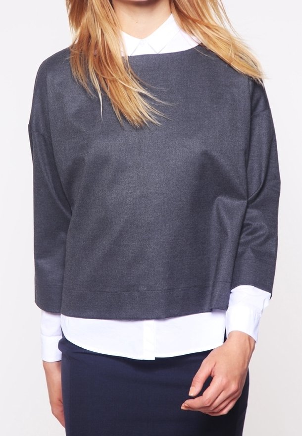 Maglione grigio accorciato con scollo rotondo, maniche lunghe e texture liscia, indossato sopra una camicia bianca con colletto. Design semplice e moderno.