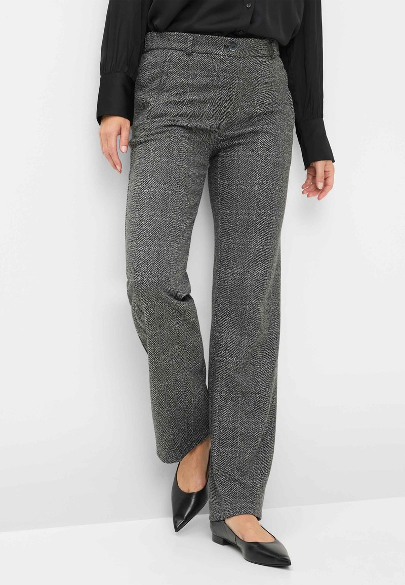 Grijze visgraatbroek met een ontspannen pasvorm en een knoopsluiting. Gepaard met zwarte puntige flats en een zwarte blouse.