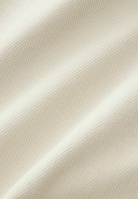 Tissu texturé beige clair avec un motif tissé subtil, présentant des ondulations douces et une surface lisse, idéal pour diverses applications.