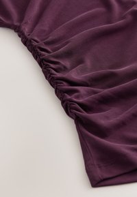 Gros plan sur un tissu violet avec des détails froncés et plissés le long d'un bord sur un fond clair.