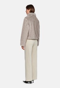 Helle beige Kunstpelzjacke mit hohem Kragen, langen Ärmeln und lockerer Passform, kombiniert mit weit geschnittenen cremefarbenen Hosen und schwarzen High Heels.