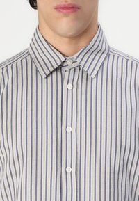 Hemd mit Kragen, das vertikale Streifen in Beige und Dunkelblau zeigt. Hergestellt aus einem leichten Stoff mit glatter Textur und Knopfleiste.