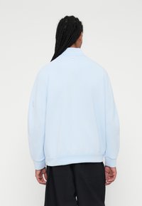 Sweatshirt azul claro com punhos e bainha canelados. Apresenta um decote redondo e um pequeno detalhe de logótipo na parte de trás. Textura de tecido suave.