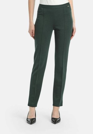 Dark green fitted trousers with a smooth texture, side seam detailing, and a slim silhouette, paired with black pointed heels.