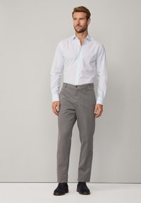 Hellblaues, knopfbares Hemd mit weicher Textur, kombiniert mit grauen, geraden Hosen und dunklen Schuhen. Schlichtes Design ohne Muster.
