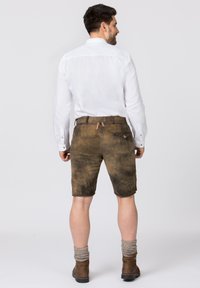 Braune Lederhosen mit einer abgenutzten Textur, einer Gesäßtasche und bindungsdetails an der Taille, kombiniert mit einem weißen Hemd mit Kragen und braunen Stiefeln.