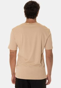 T-shirt beige a maniche corte realizzato in tessuto morbido. Vestibilità rilassata con collo giro e orlo dritto, con una minima presenza di branding sulla manica.