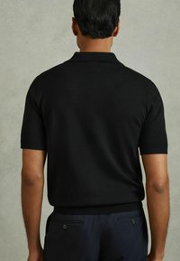 Svart kortärmad polo-skjorta med rak fåll, tillverkad av ett slätt tyg, med klassisk krage och fint stickad textur.