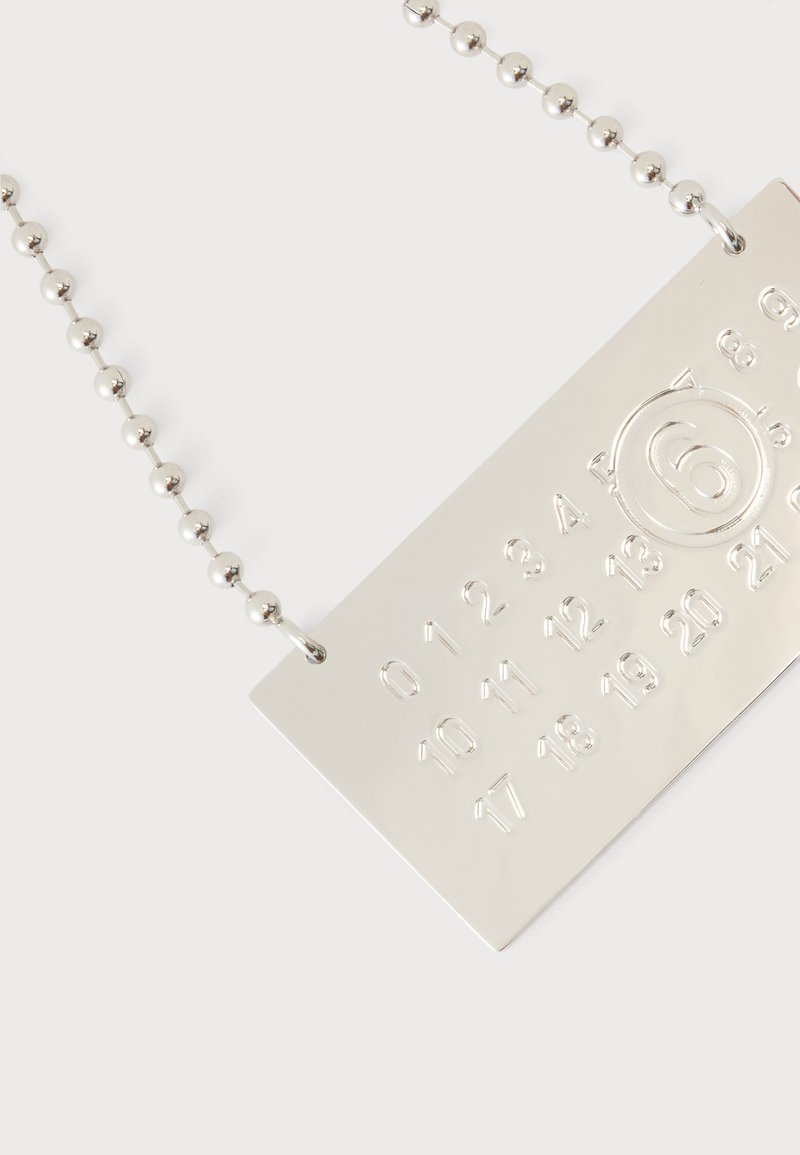 Ciondolo rettangolare in argento con numeri in rilievo da 0 a 23 in file, il numero 6 è cerchiato, appeso a una collana con catena a palline in argento.