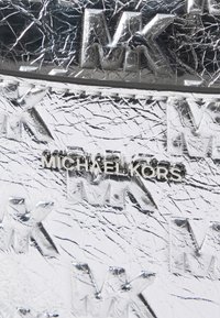 Sølv strukturerte materiale med hevet "MK" mønster og sølv "MICHAEL KORS" logo som er tydelig plassert i midten.