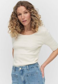 Witte, kortebloezende top met horizontale, textuurstripes; ronde halslijn; gecombineerd met lichtblauwe denim jeans met voorzakken.