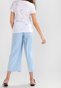 Bílý tričko s krátkým rukávem a metalickými vzory ananasů, zkombinované se světle modrými širokými kalhotami a černými lodičkami na podpatku.