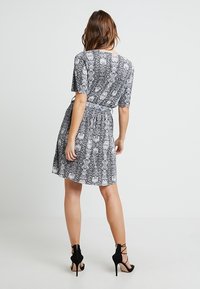 Vestido de serpiente en blanco y negro con mangas cortas y cinturilla anudada, que presenta una falda acampanada y una textura de tela ligera.