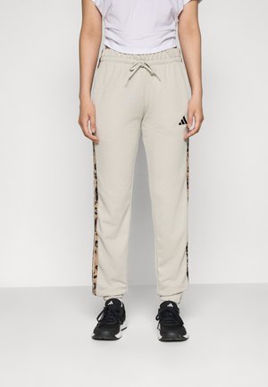 Beige sweatpants med elastisk midje, sider med leopardmønster striper, og avkuttede ankler. Kombinert med svarte sneakers med hvite detaljer.