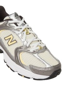 Zapatilla de running con parte superior de malla plateada y blanca, acentos amarillos, suela blanca gruesa y cordones planos blancos. Detalles texturizados en los lados.