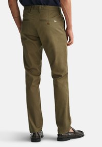 Pantalones verde oliva de corte recto, hechos de algodón. Presentan dos bolsillos traseros, uno con cierre de botón y un acento metálico.