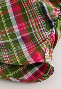 Tissu à carreaux vert, rouge et rose avec un détail de couture froncée sur un côté, montrant un gros plan de la texture et du motif du textile.