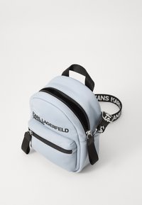 Svetlomodrý mini batoh vyrobený z hladkého materiálu. Má dva zipsové oddiely, hornú rukoväť a nastaviteľný čierny popruh s logom.