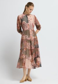 Dlouhá, vícevrstvá šaty s kombinací paisley a geometrických vzorů v růžové, černé a béžové barvě. Průsvitná látka, tříčtvrteční rukávy a knoflíky.