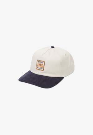 Caps med en kremfarget krone og marineblå kordfløyelsbrem. Har et firkantet logopatch med oransje og blå detaljer på forsiden.