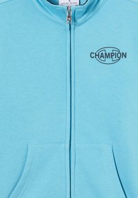 Felpa con zip di colore blu chiaro, con scollo rotondo, tasche anteriori e logo nero "CHAMPION" sul lato sinistro. Tessuto dalla texture liscia.