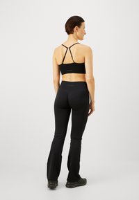 Sujetador deportivo negro con un diseño de espalda cruzada, leggings negros ajustados de cintura alta y zapatos deportivos negros, mostrando una textura suave y elegante.