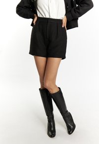 Pantaloni corti neri a vita alta con una trama a diamante e due tasche frontali, abbinati a stivali in pelle nera al ginocchio.