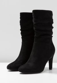 Bottes noires en daim à la cheville avec un design décontracté, un bout pointu et un talon haut. Texture lisse, sans quincaillerie visible ni motifs.