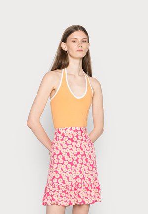 Top halter laranja com acabamento branco, combinado com uma saia rosa com padrões de margaridas brancas e um acabamento em babados.