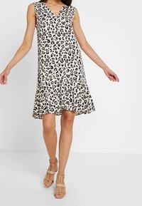 Ärmelloses Kleid mit Leopardenmuster, V-Ausschnitt, fließendem Saum und leichtem Stoff. Kombiniert mit nudefarbenen Riemchensandalen für den Kontrast.