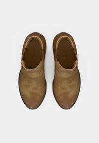 Bottes basses en cuir marron à texture lisse, bout arrondi et panneaux latéraux élastiques. Semelle extérieure en caoutchouc noir crantée.