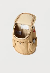 Μικρό μπεζ σακίδιο με ανοιχτό το κύριο διαμέρισμα, εξωτερική τσέπη με φερμουάρ και ελαστικές πλαϊνές τσέπες σε απλό λευκό φόντο.